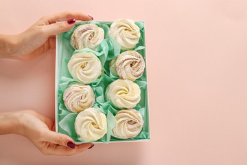 Box with homemade marshmallows in female hands on a pastel background, horizontal orientation, Top view