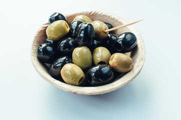 Olives of black and green variety in a palm leaf bowl on white background