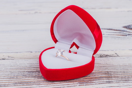 Golden ring in red box on wooden background. Diamond ring in a heart-shaped box. Marriage proposal concept.