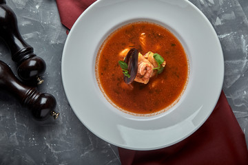 Fresh seafood soup in a white plate on dark background, top view