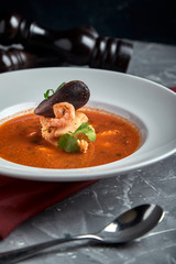 Fresh seafood soup in a white plate on dark background, top view