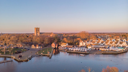 An aerial view of a river at golden hour with grassy bank and majestic church and marina in the background under a majestic blue sky - obrazy, fototapety, plakaty