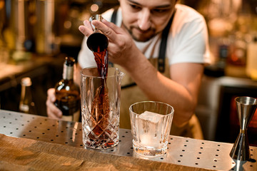 Bartender pouring a brown alcoholic drink from the jigger to a mixing glass