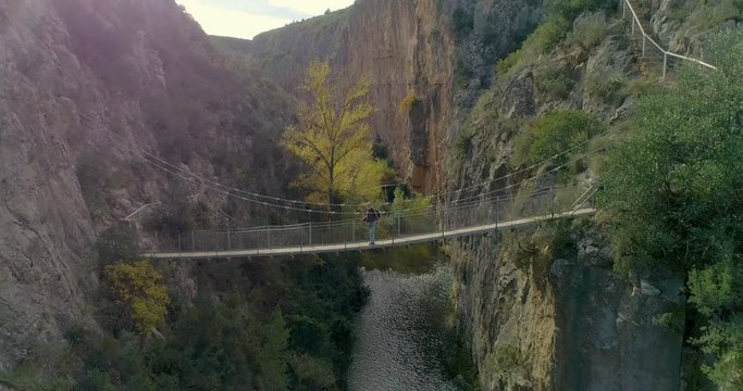 Vuelo hacia atr&aacute;s de dron desde puente colgante y senior caminante