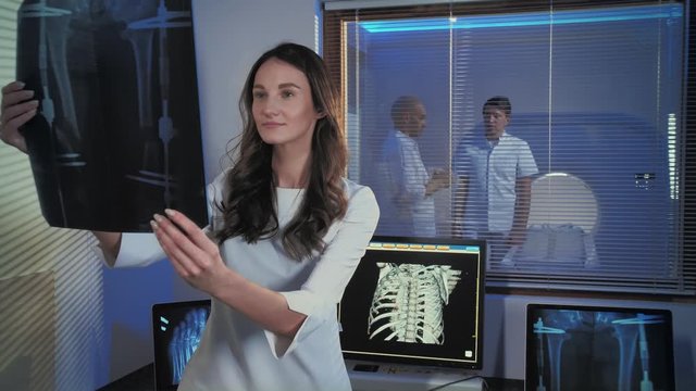A picture of a beautiful young woman doctor. The doctor is standing in the tomography room and studying the x-ray picture. Professional people at work.