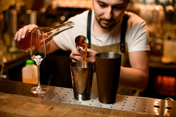 Bartender pouring an orange alcoholic drink from the jigger to a brown steel shaker