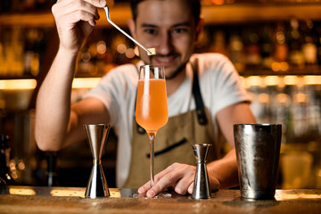Professional bartender adding with tweezers a little sugar cube to a cocktail in the glass