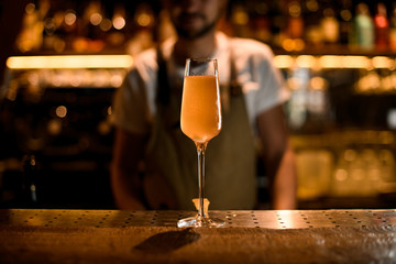 Professional male bartender serving orange yellow cocktail in the tall glass