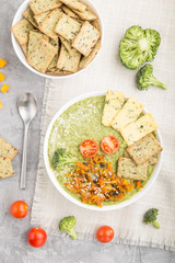 Green broccoli cream soup with crackers in white bowl on a gray concrete background,  top view.