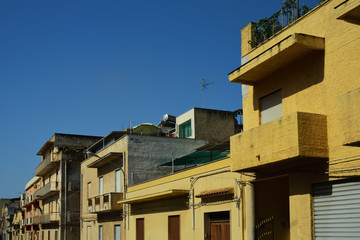 Typical row of flat houses in the middle of a city at the roadside on Sicily in Italy in summer with closed windows against blue sky in the heat of the day
