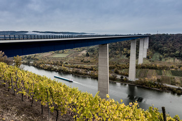 Barge transports shipping under high bridge travel along Rhine river, Wine yards Germany 