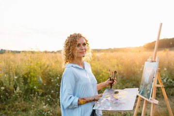 Pretty woman is painting. Open air session. Cute woman draws a picture at sunset. girl artist