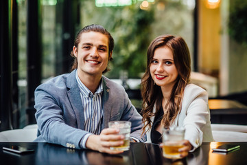 Lovely concept, pretty young and cheerful couple with drinks on hands spend time at modern restaurant.