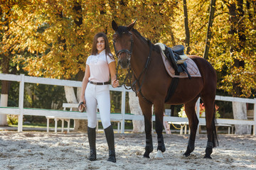 Young woman posing with wild horse in the field against the autumn forest.