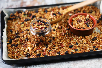 Freshly made homemade granola on a baking sheet. Granola in a wooden spoon and in a jar. Selective focus. Healthy diet concept. Keto diet.