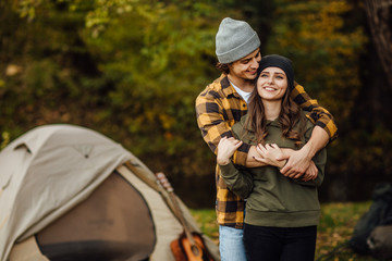 Happy loving couple of tourist in the forest near tent. A handsome man hugs an attractive woman.