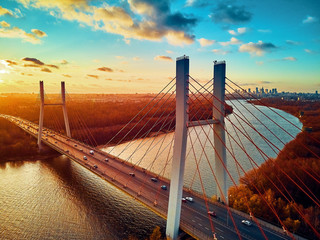 Beautiful panoramic aerial drone view to cable-stayed Siekierkowski Bridge over the Vistula river and Warsaw City skyscrapers, Poland in gold red autumn colors in November evening at sunset