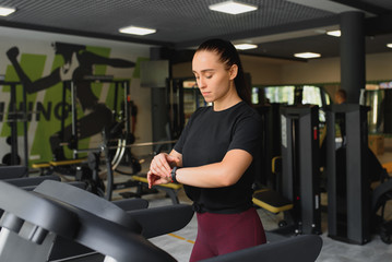 Fototapeta premium Woman trains on a treadmill in the gym. Young fitness girl running on treadmill machine. Sports exercises for weight loss.