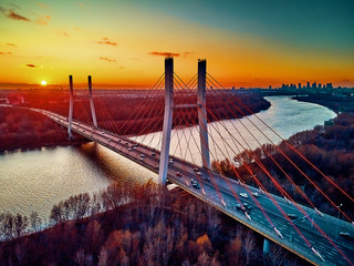 Beautiful panoramic aerial drone view to cable-stayed Siekierkowski Bridge over the Vistula river and Warsaw City skyscrapers, Poland in gold red autumn colors in November evening at sunset