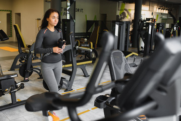 Young woman drinking water and taking a break after workout in gym,