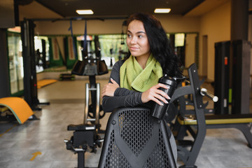 Fototapeta na wymiar Young woman drinking water and taking a break after workout in gym,