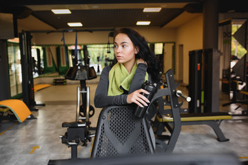 Fototapeta na wymiar Young woman drinking water and taking a break after workout in gym,
