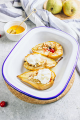 Sweet baked pears with honey, nuts, cranberries and cinnamon in enameled baking bowl on stone background. Top view. Flat lay