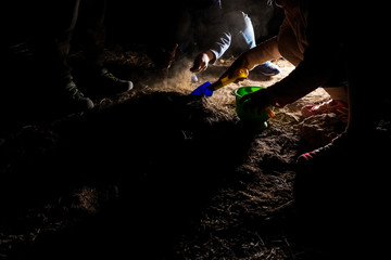 Children play with the earth one night in the light of a large lantern, dark image.