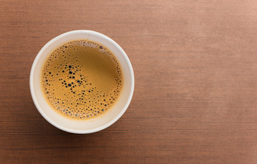 Top view of paper cup of black coffee on brown wooden table