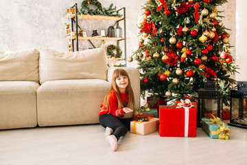 Obraz na płótnie Canvas Smiling girl playing near Christmas tree and gifts