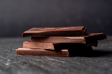 Broken pieces of dark bitter chocolate on black stone surface. Dark background.