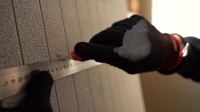 Close up hands worker in black and red gloves using metal ruler cuts sheet of thermal insulation gray color.