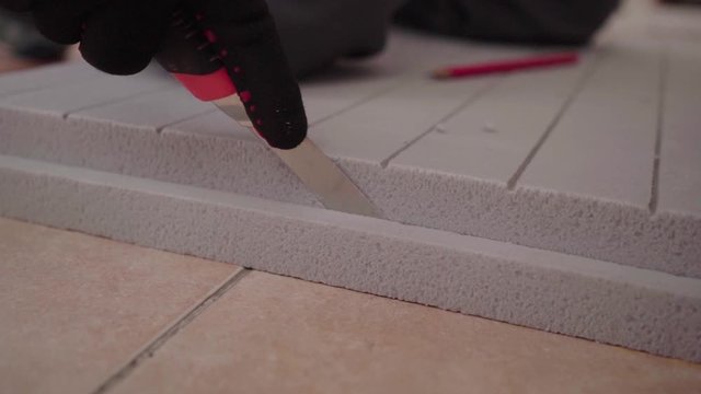 Close up hands worker in black and red gloves using metal ruler cuts sheet of thermal insulation gray color.
