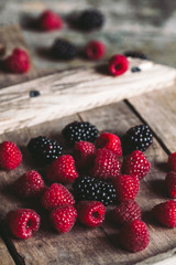 blackberries and raspberries on a cutting board. wooden background, vintage style