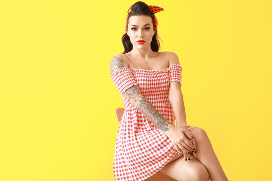 Portrait of beautiful tattooed pin-up woman sitting on chair against color background