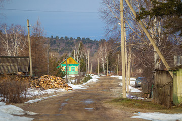 Fototapeta na wymiar Russian village. Bad dirt road in the middle of a Russian village on the background of wooden houses and a fence. Dirty rural road in the spring in puddles.