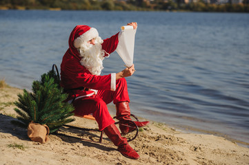 christmas, holidays, travel and people concept - man in costume of santa claus reading letter