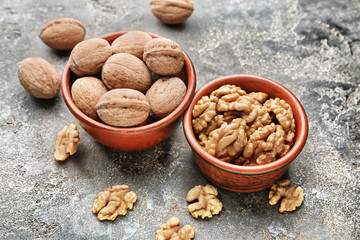 Bowls with tasty walnuts on grey background