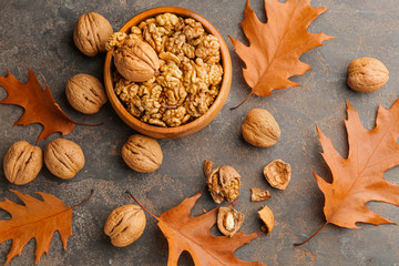 Bowl with tasty walnuts and autumn leaves on grey background