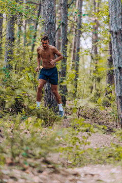 Male shirtless joger running in mountains under trees