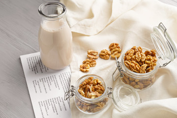 Jars with tasty walnuts and bottle of milk on table