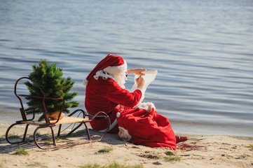 christmas, holidays, travel and people concept - man in costume of santa claus reading letter