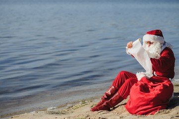 christmas, holidays, travel and people concept - man in costume of santa claus reading letter