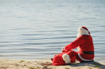 Santa Claus walking along the beach holding a sack of presents with copyspace with clouds and sky