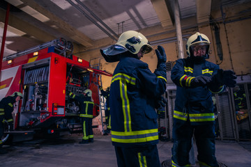 Firefighters preparing their uniform and the firetruck in the background inside the fire station