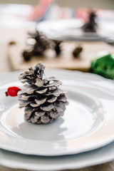 Christmas table setting with rustic details in natural and white tones. Dining place decorated with pine cones, branches and candles