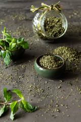 Dried peppermint in a bowl and a bunch of fresh mint, on gray background.