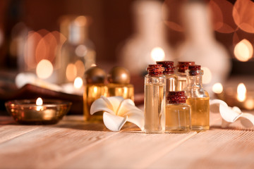 Bottles of essential oil and flowers on table in spa salon