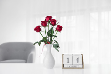 Calendar with date of Valentine's Day and roses on table in room