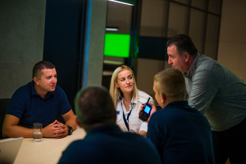 Security guard monitoring modern CCTV cameras in a surveillance room. Group of security guards sitting and having conversation.